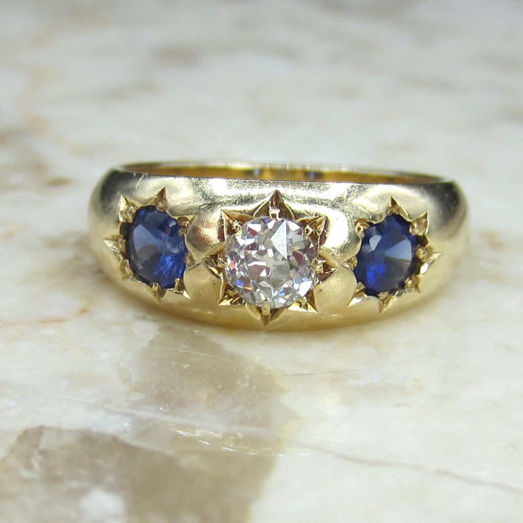 Antique 18k gold ring with a central diamond and two sapphire stars on a marble surface.