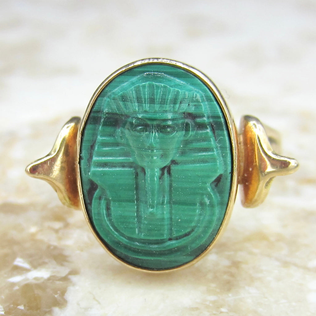 Gold ring with a green stone featuring an engraved design on a textured beige background