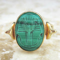 Gold ring with a green stone featuring an engraved design on a textured beige background