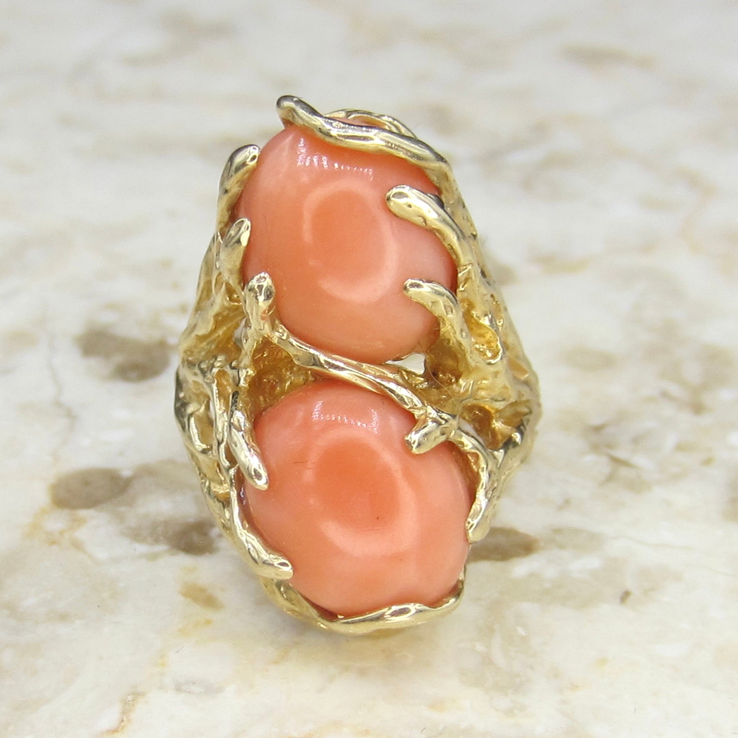 Gold ring with coral stones on a marble surface