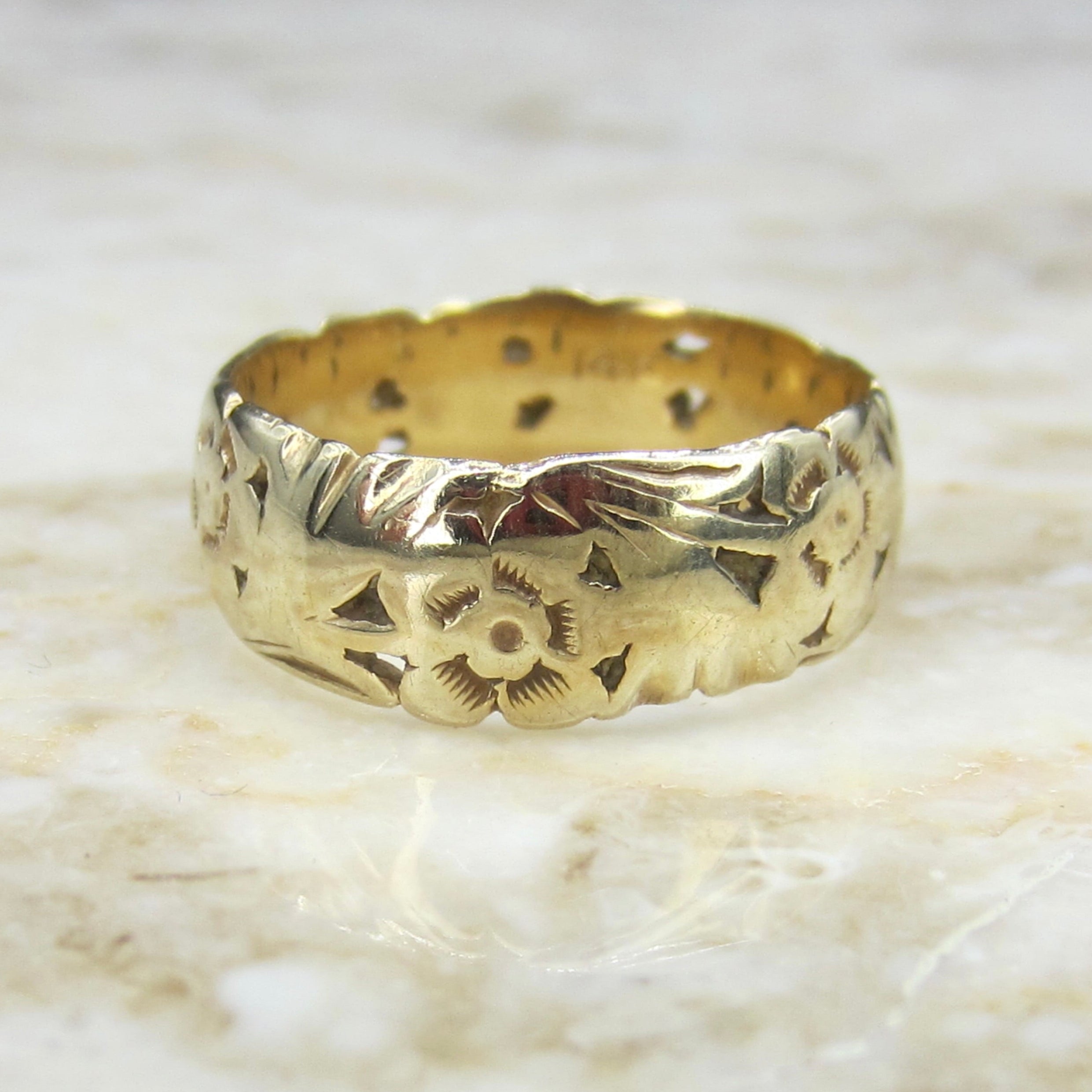 Gold ring with intricate designs on a marble surface