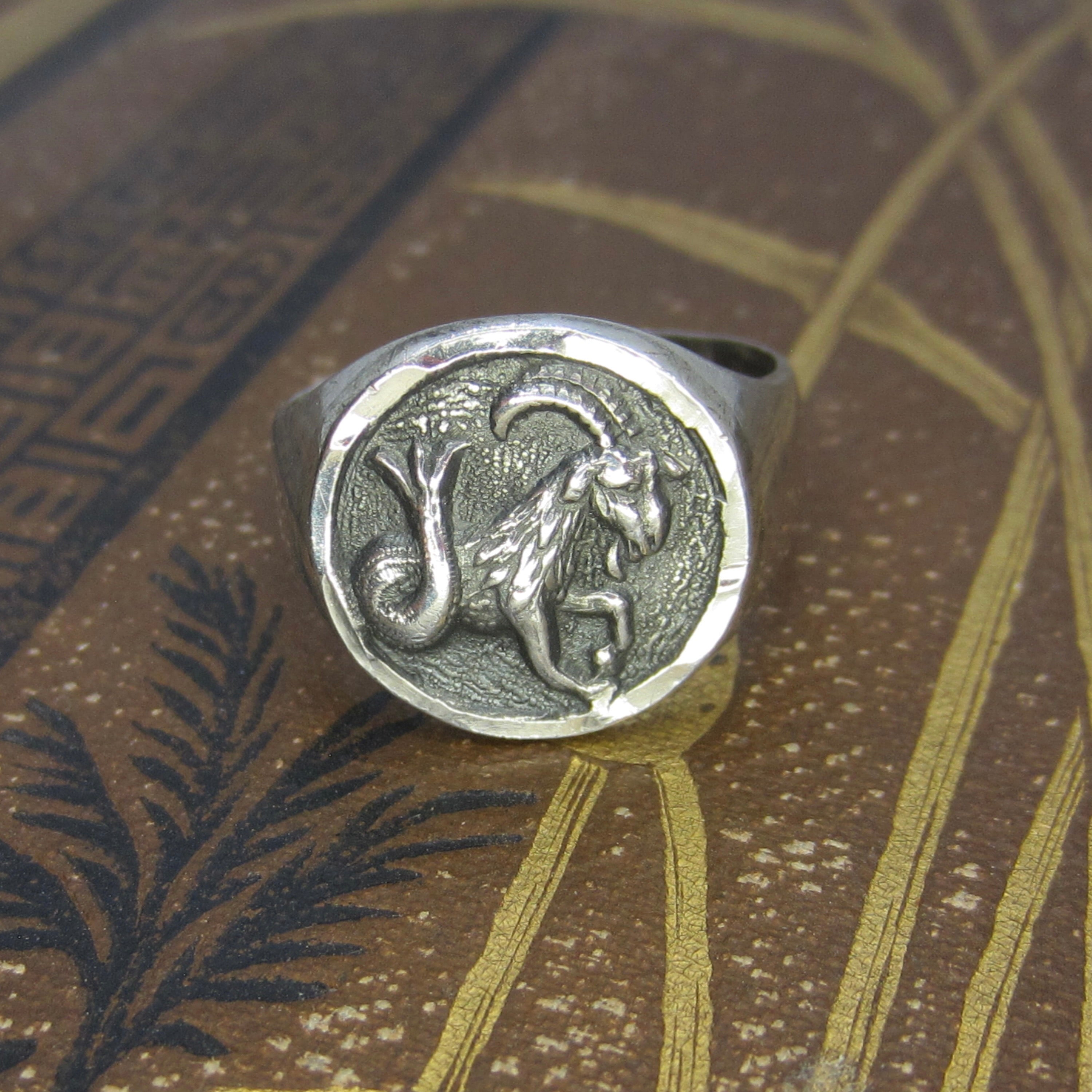 Silver ring with a goat emblem on a textured surface