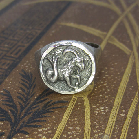 Silver ring with a goat emblem on a textured surface