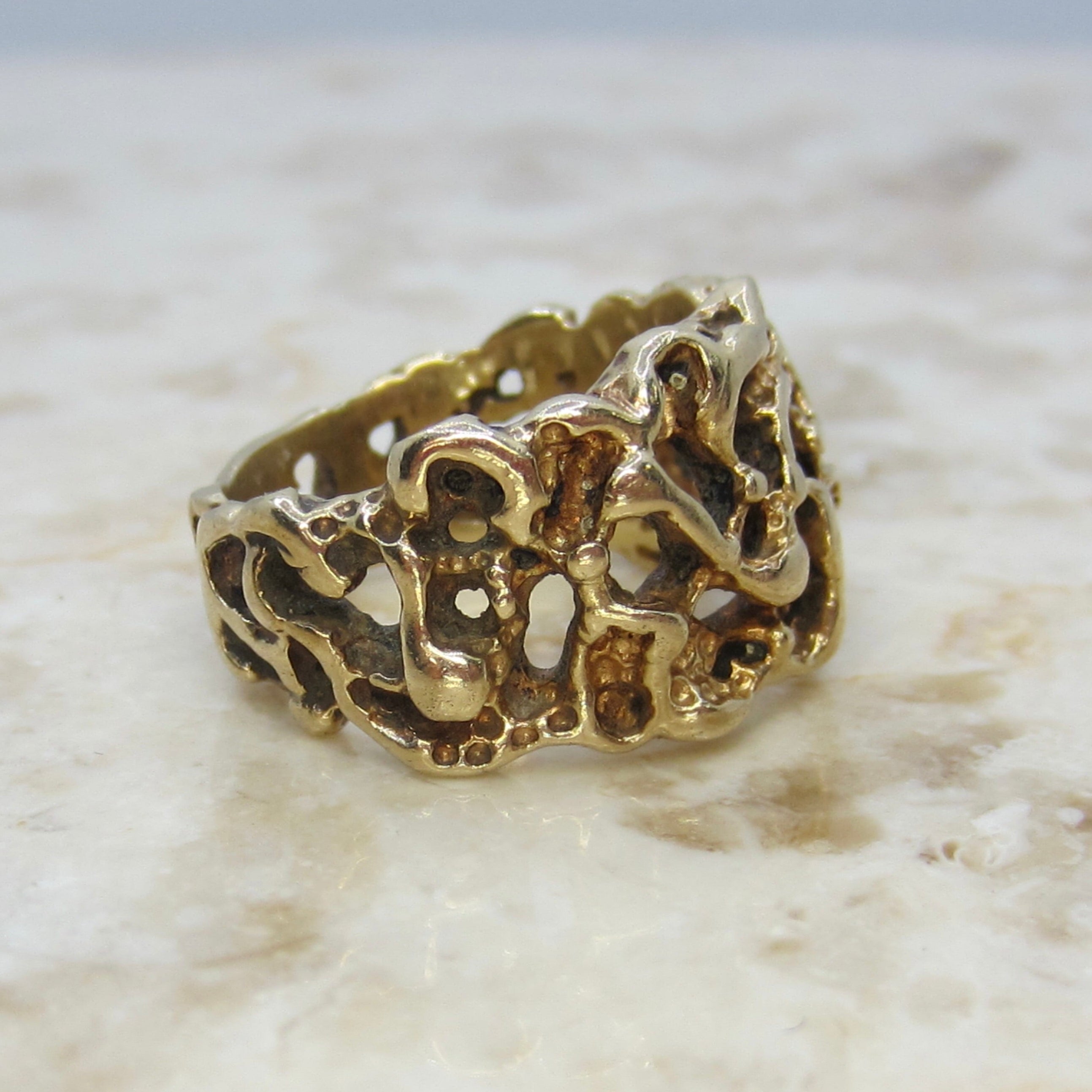 Gold ring with intricate design on a marble surface
