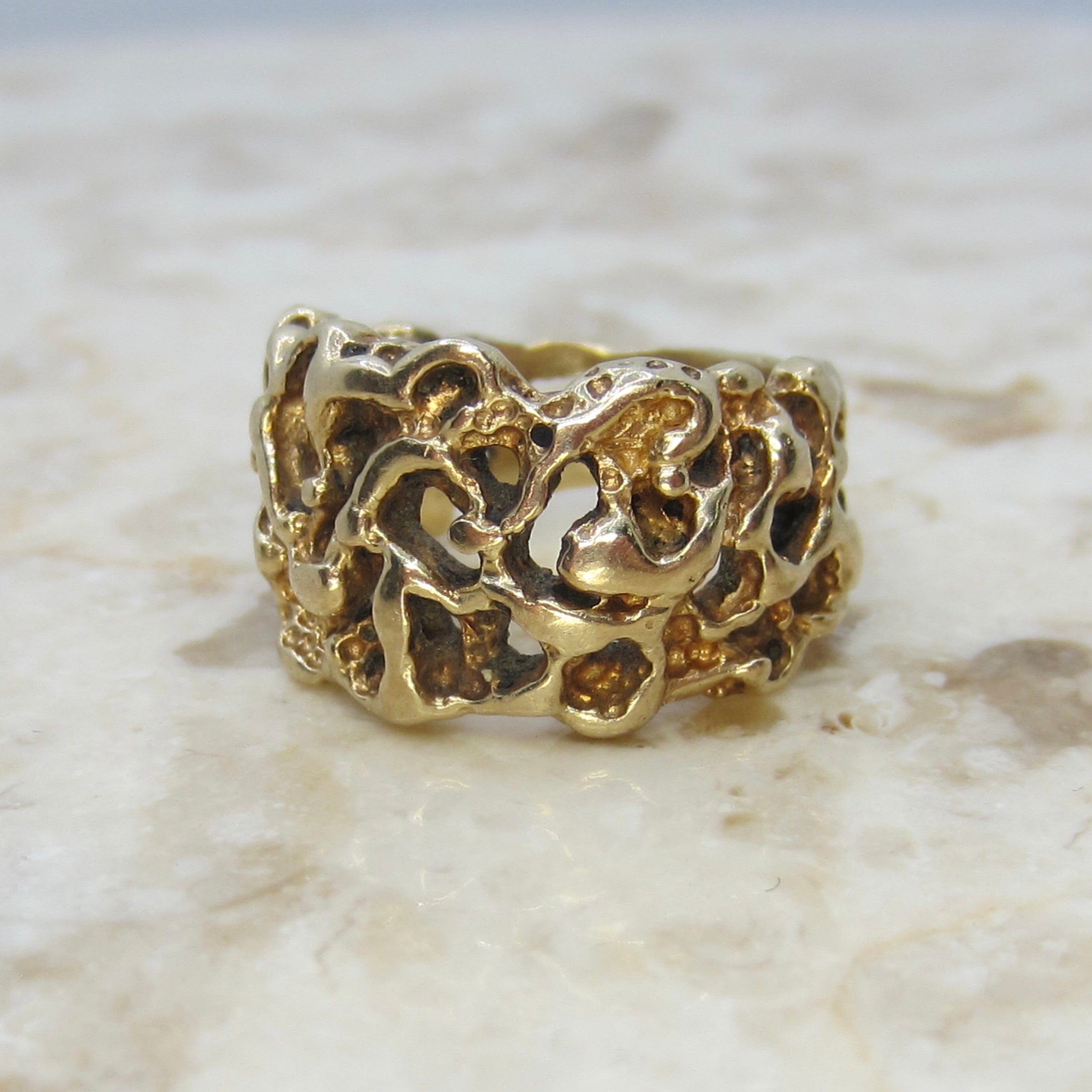 Gold ring with intricate design on a marble surface