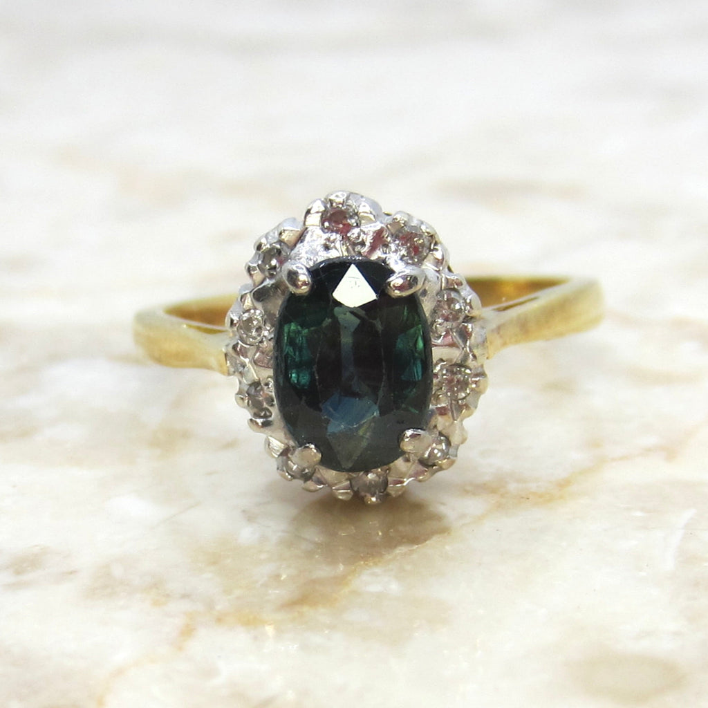 Gold ring with a green gemstone and diamond halo on a marble surface