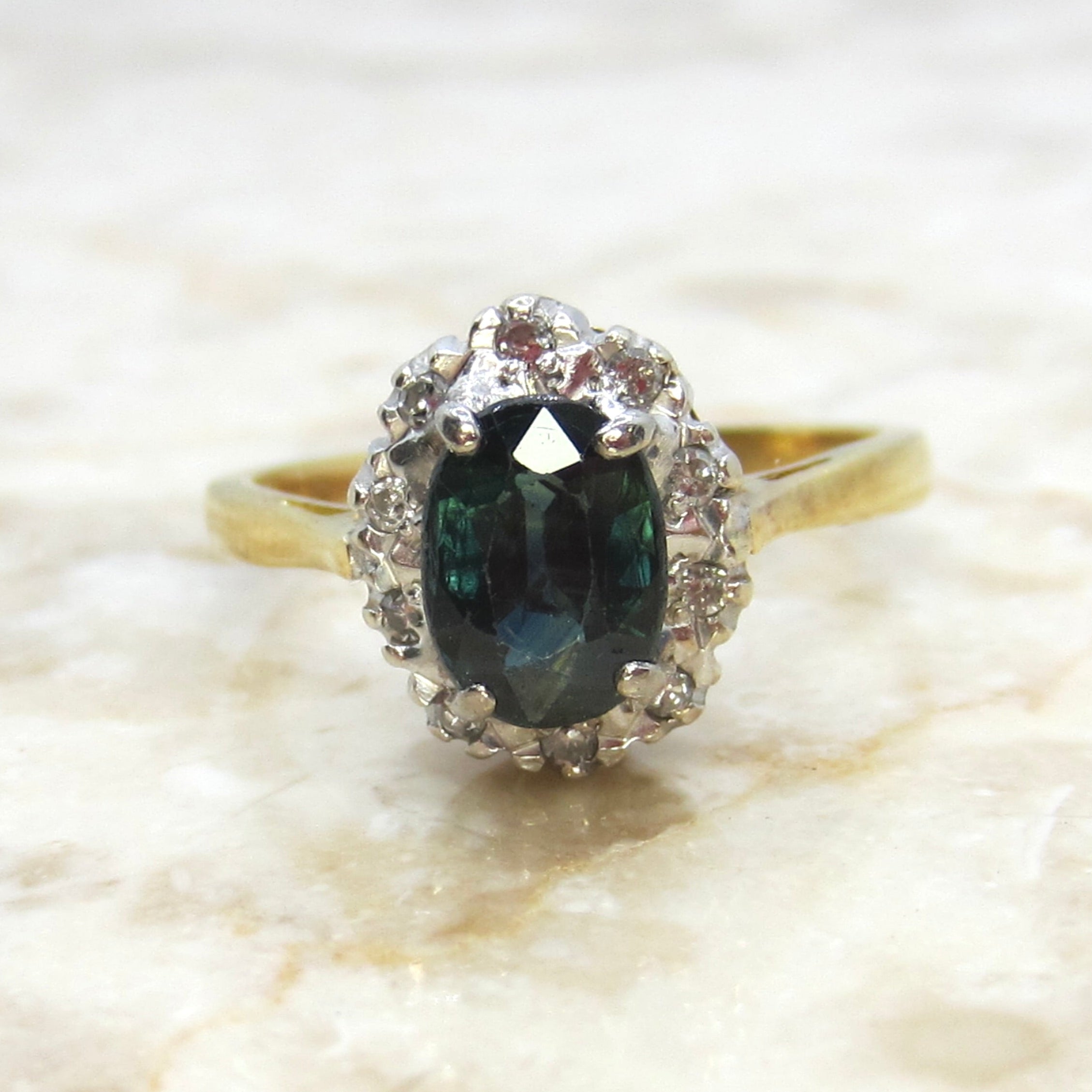 Gold ring with a green gemstone and diamond halo on a marble surface