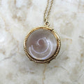 Gold necklace with a round pendant on a marble surface