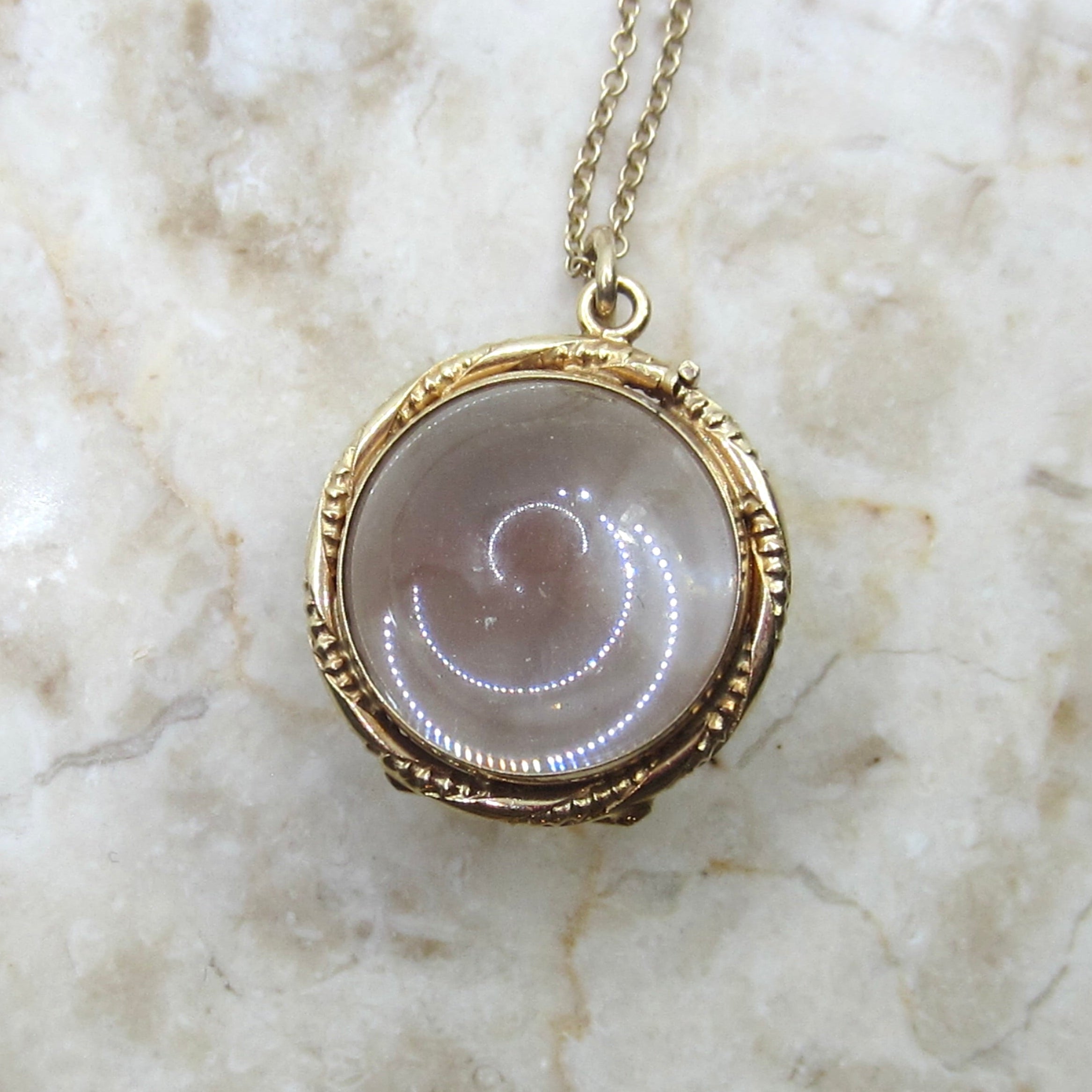 Gold necklace with a round pendant on a marble surface