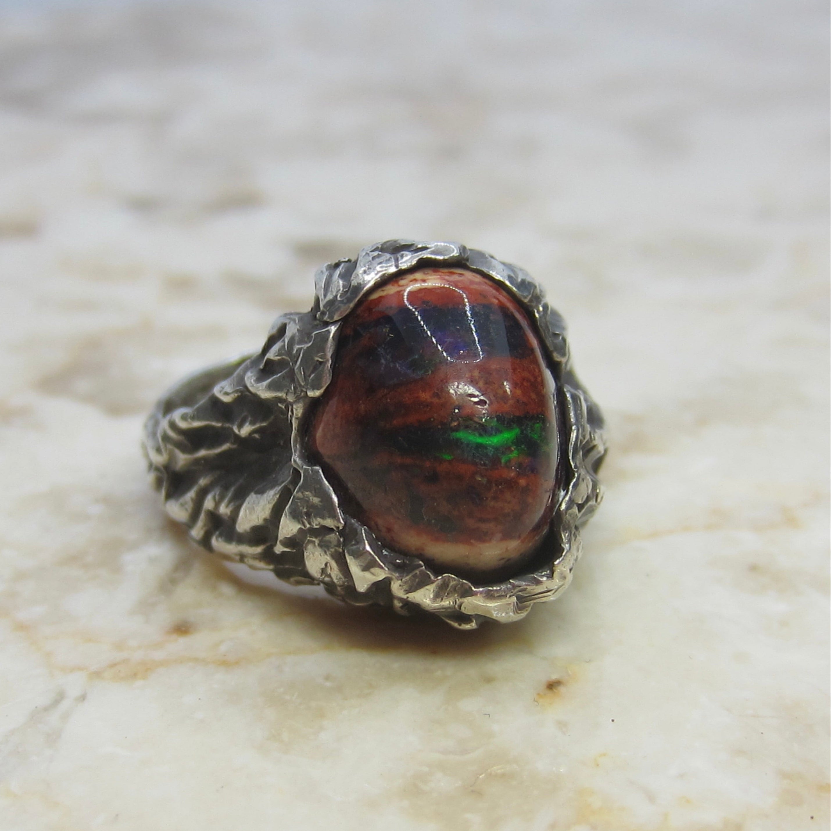 Silver ring with a colorful stone on a marble surface