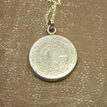 Silver coin pendant on a chain against a textured brown background