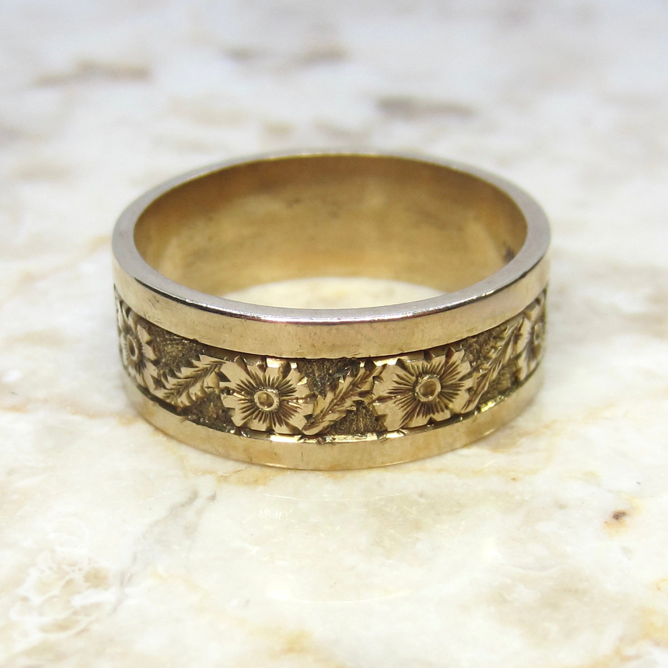 Gold ring with floral engraving on a textured beige background