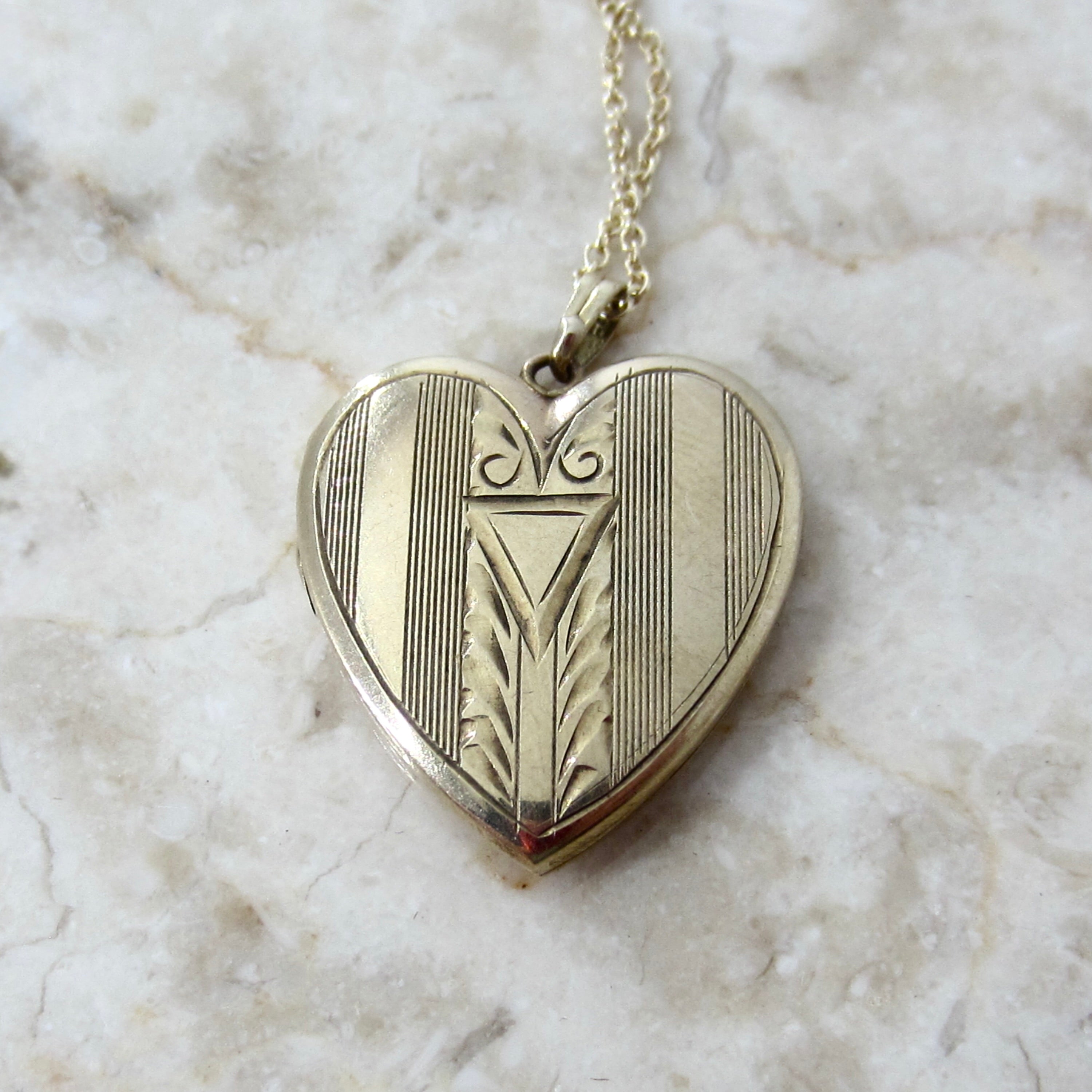 Heart-shaped silver locket with intricate designs on a marble surface