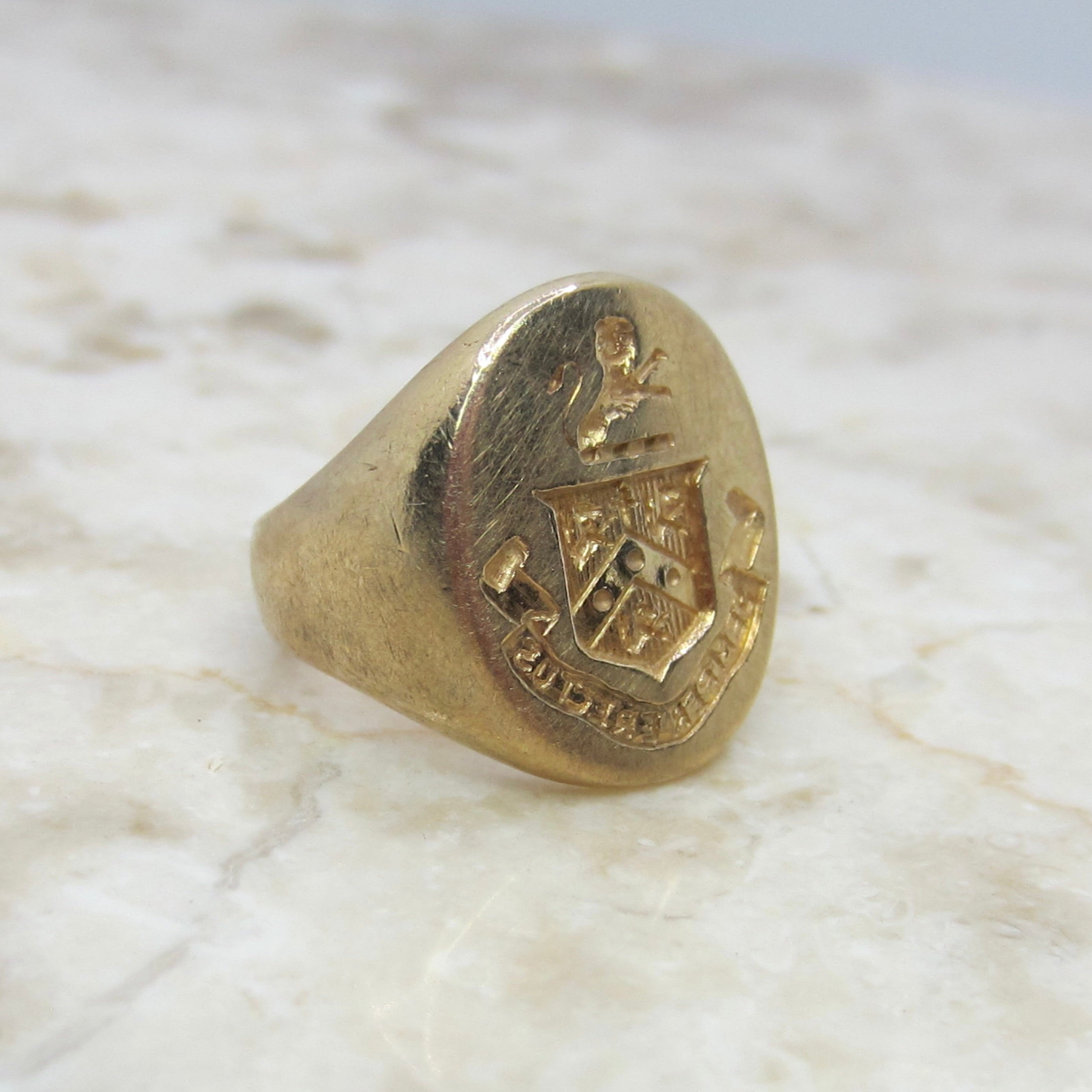 Gold ring with a crest design on a marble surface