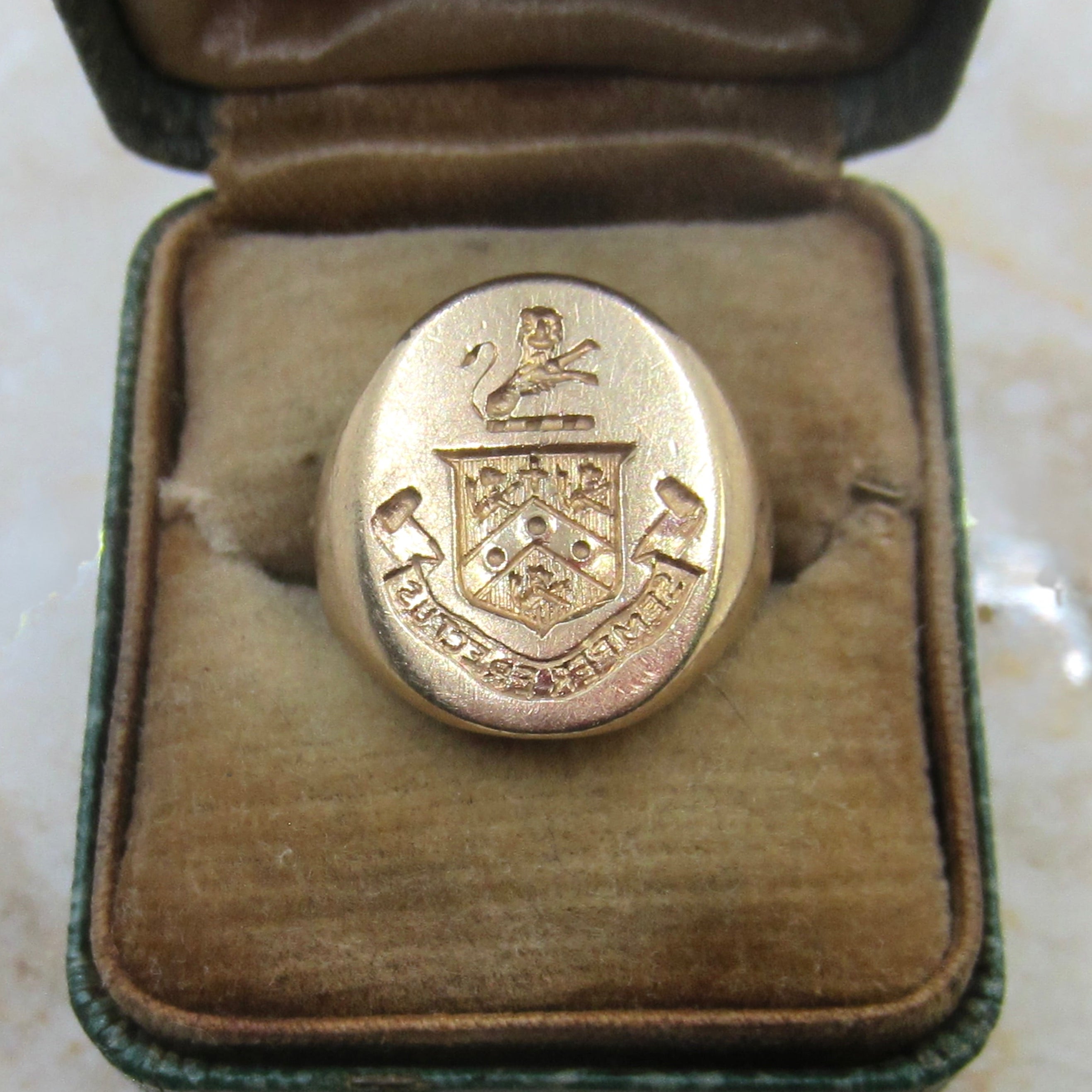 Gold ring with a coat of arms design in an open jewelry box on a marble surface