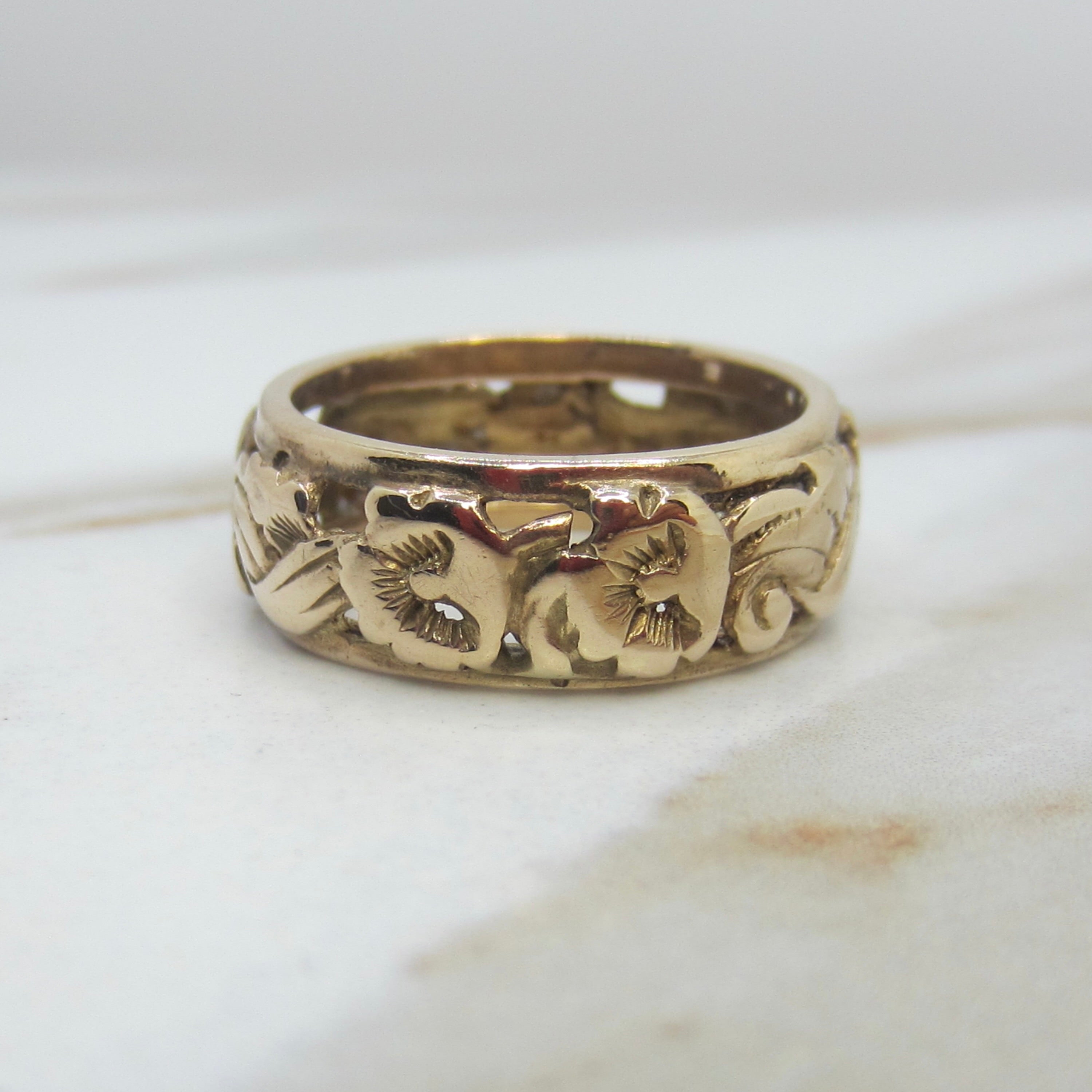 Gold ring with floral engraving on a marble surface