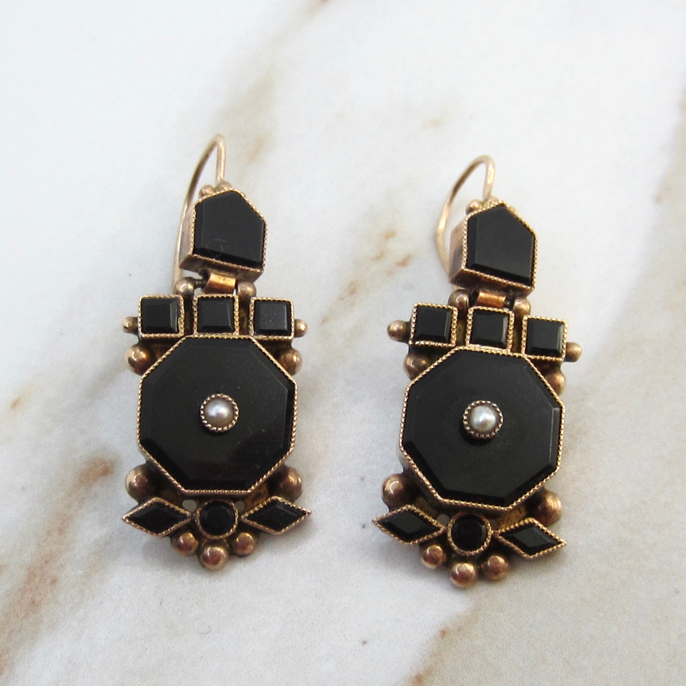 Pair of black and gold earrings on a marble surface