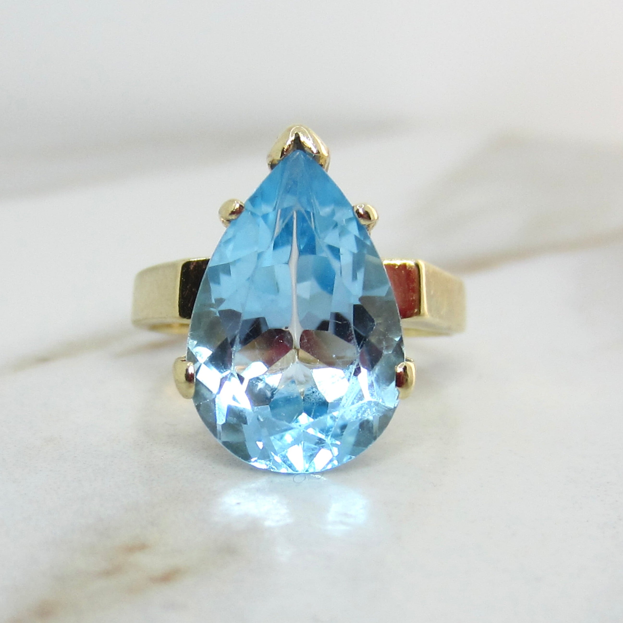 Gold ring with a large blue teardrop-shaped gemstone on a marble surface