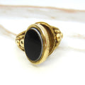 Decorative ring with black stone and gold band on a white background