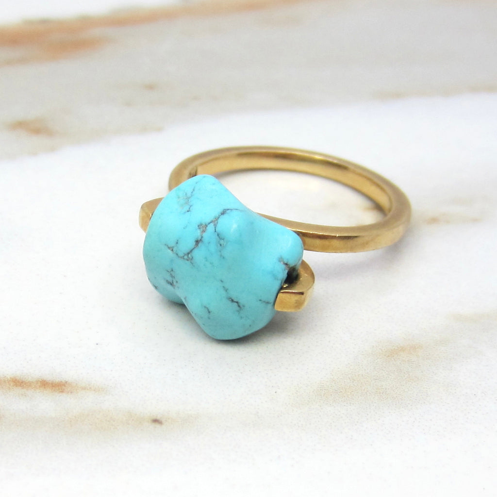 Gold ring with a turquoise stone on a marble surface