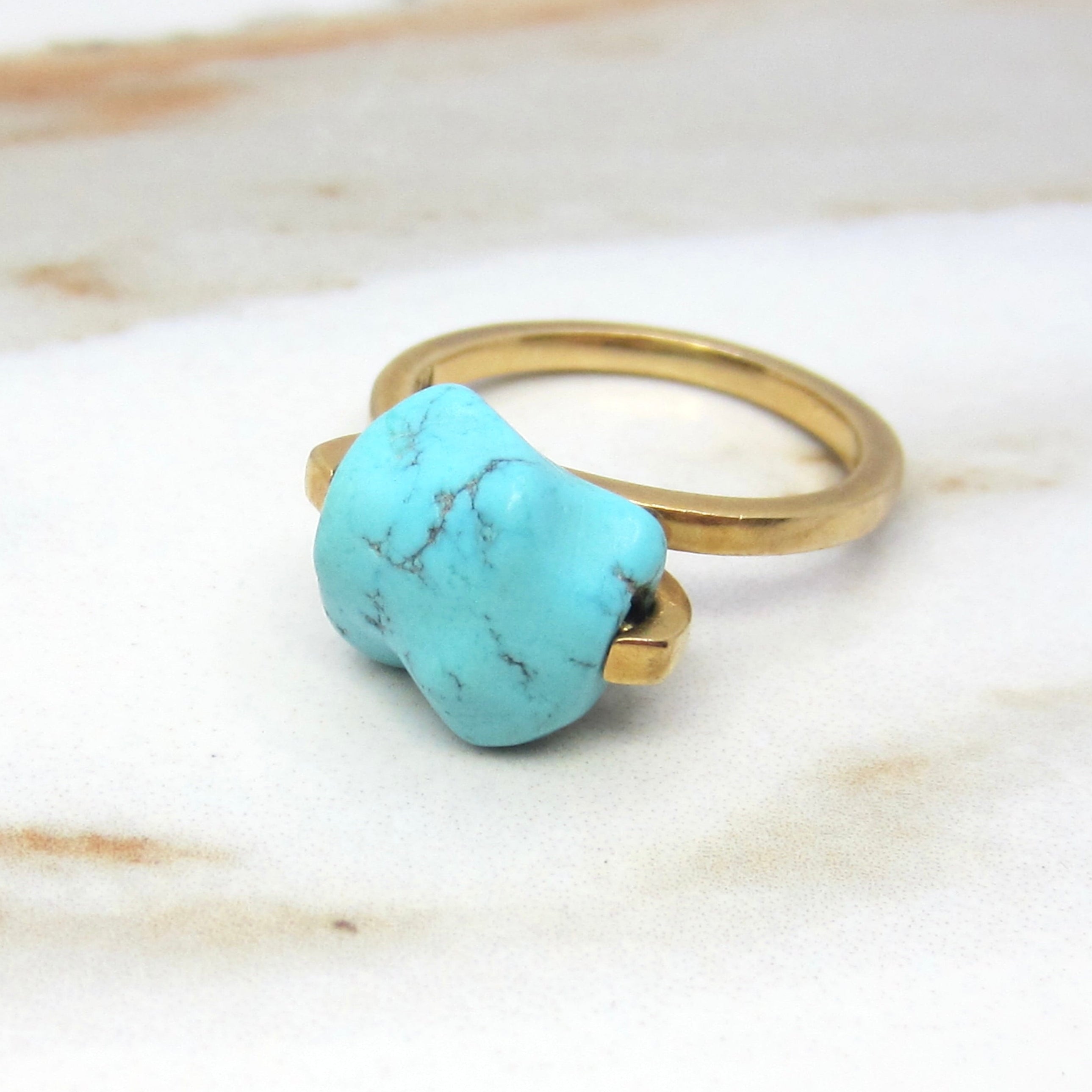 Gold ring with a turquoise stone on a marble surface