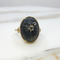 A vintage gold ring featuring an oval black cabochon stone carved with ancient hieroglyphic symbols, resting on a white marble surface.