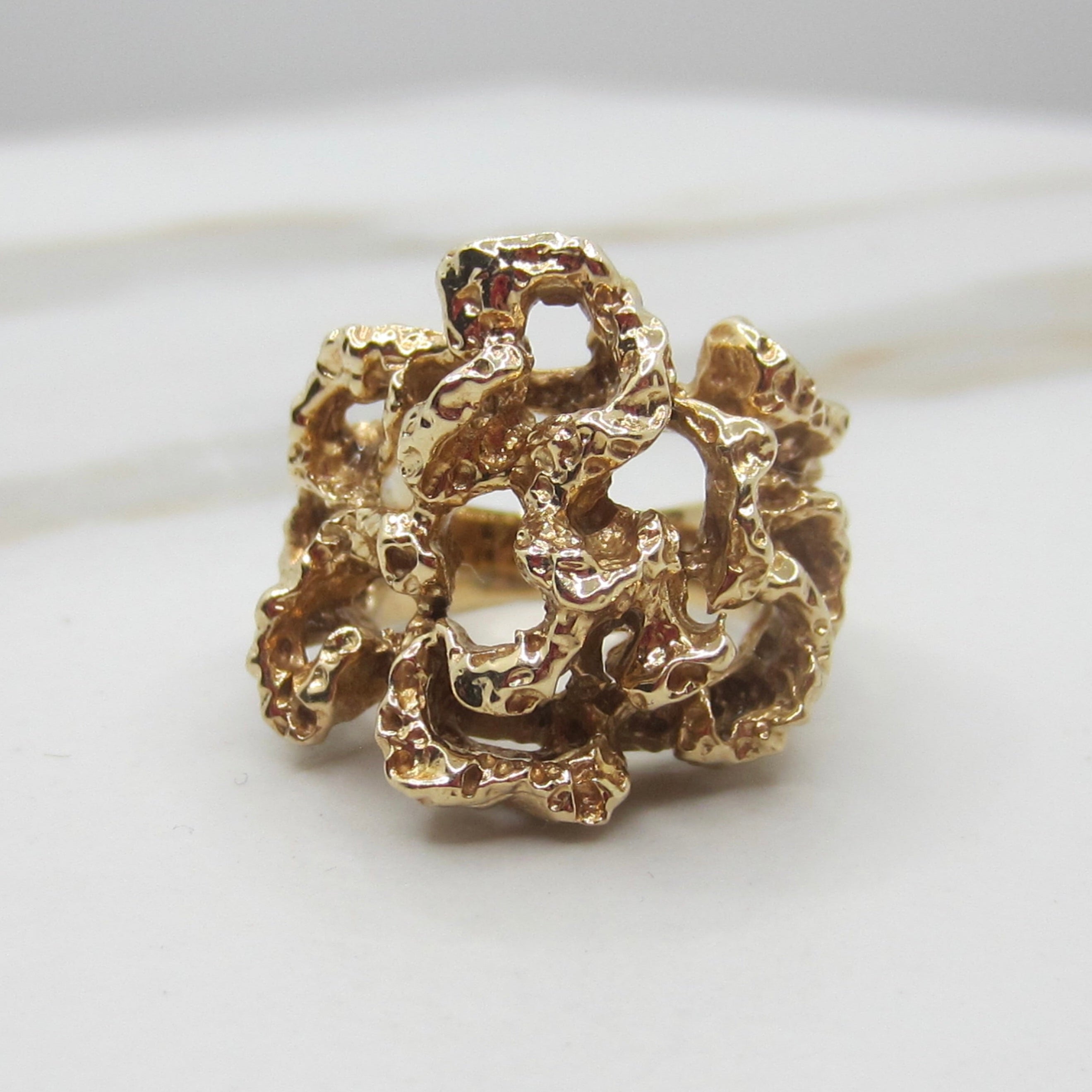 A gold ring with an organic, coral-like textured design, photographed on a light gray and white marble surface.