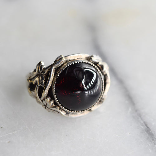 Antique Art Nouveau silver ring with a red garnet cabochon in the center and leaf patterns around it.