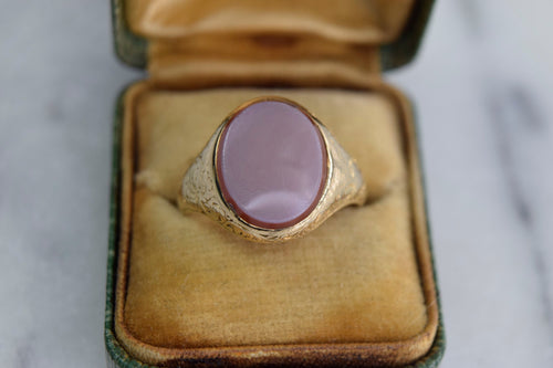 An antique 18k gold signet ring with a purple Sardonyx stone, hand-engraved with a scrolling design, displayed in its case.
