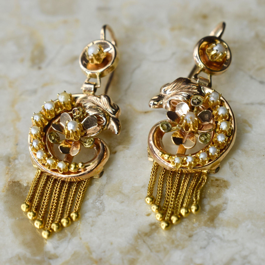 A pair of antique Victorian 14k gold swan earrings with seed pearls, featuring a floral design and tassel detailing.