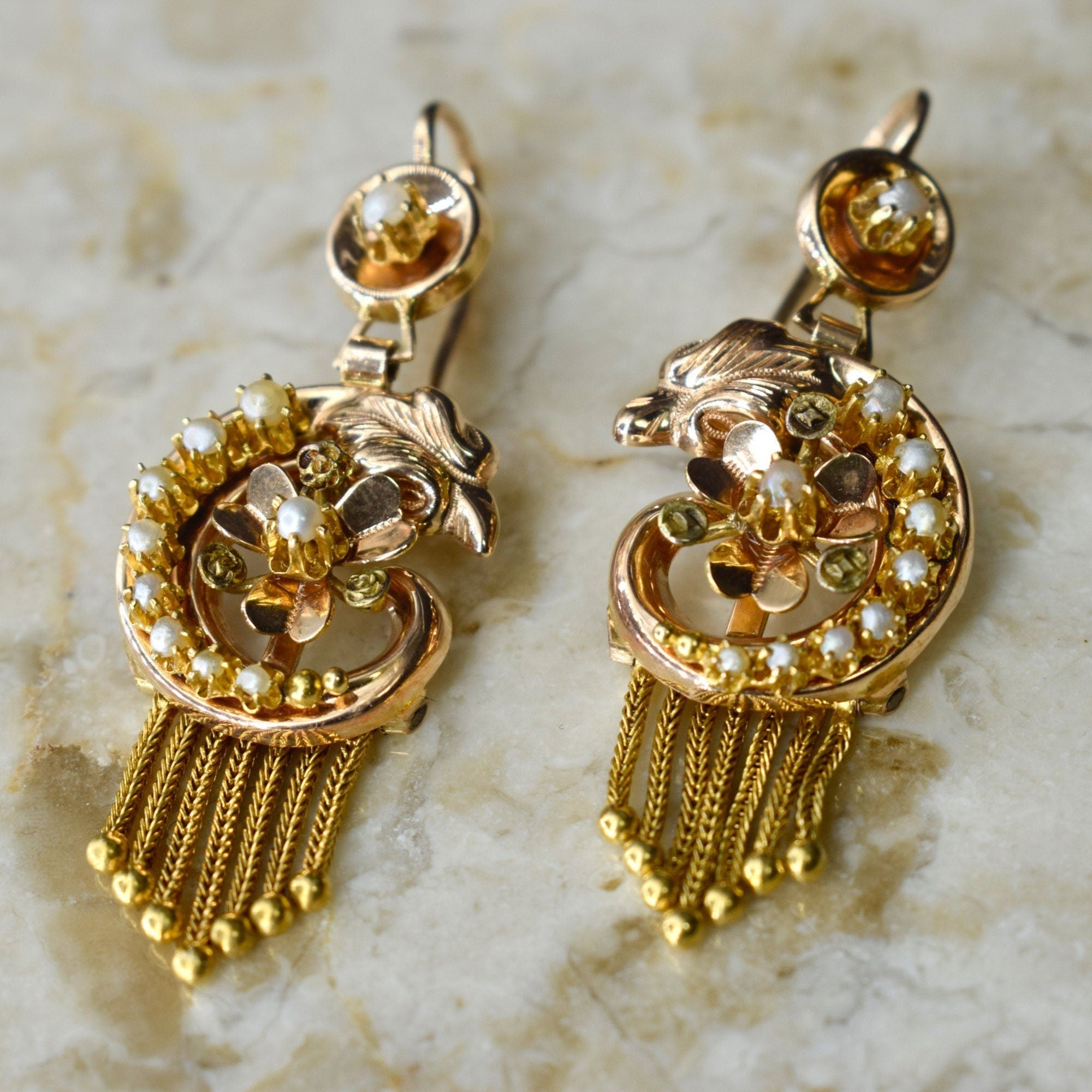 A pair of antique Victorian 14k gold swan earrings with seed pearls, featuring a floral design and tassel detailing.
